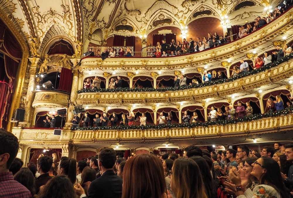 Mentorat - Vue des balcons d'une salle d'opéra avec le parterre et les gens du haut debout