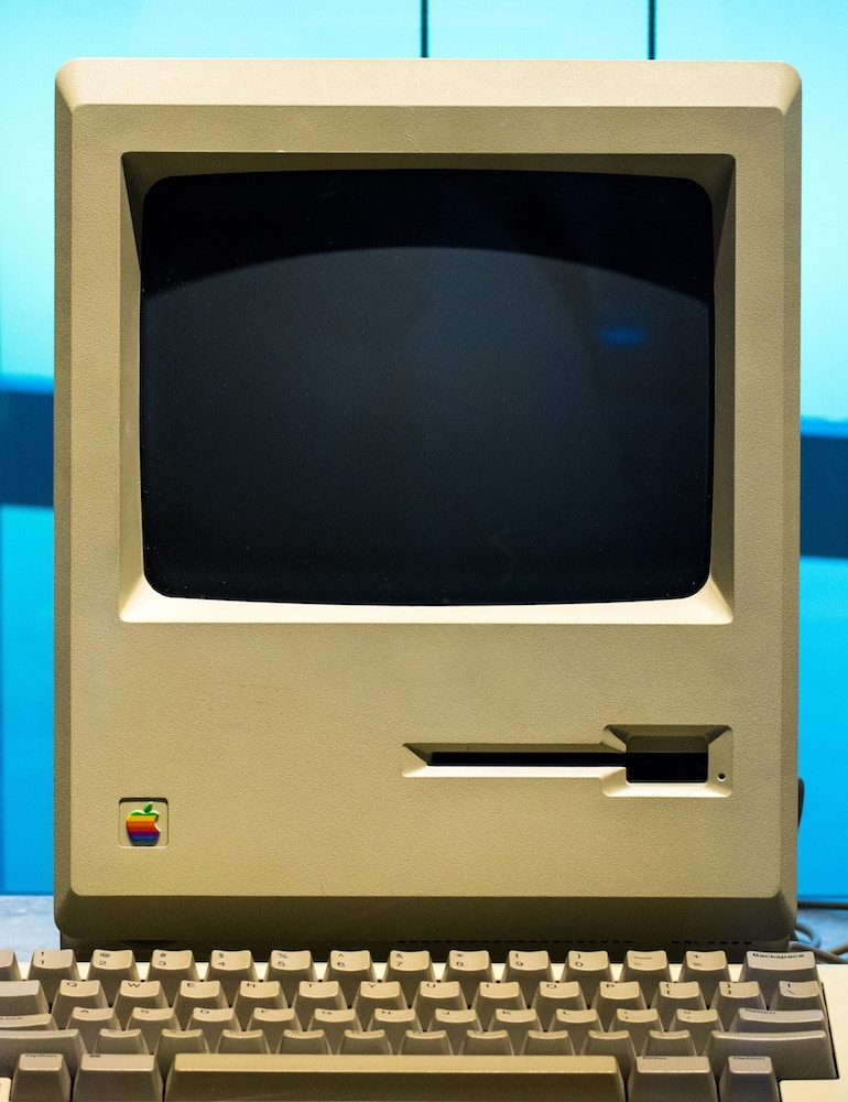Tirer avantage - Vieil ordinateur Macintosh jauni par le temps placé devant un fond bleu