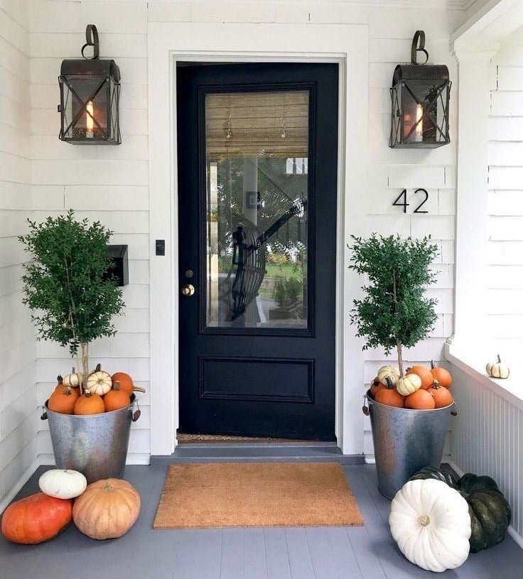 astuces déco pour une entée extérieure avec une porte foncée, des lumières et des citrouilles en décoration