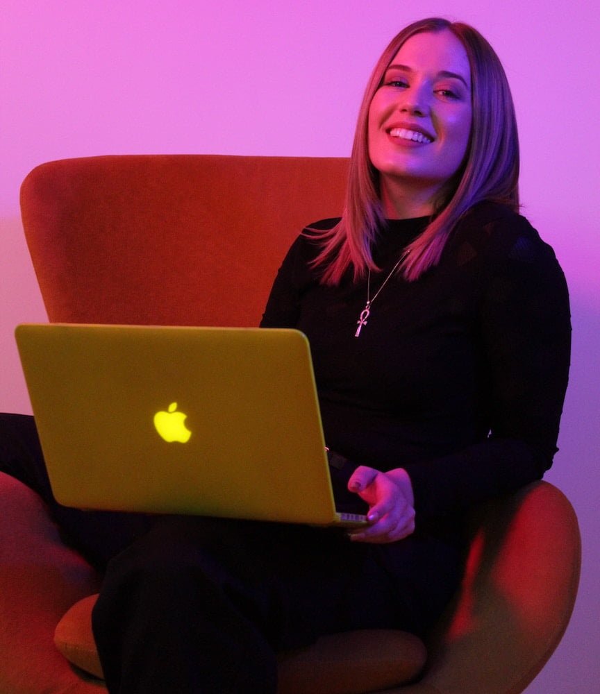 Femme assise dans un fauteuil rouge avec un ordinateur portable sur ses jambes avec un filtre mauve (créativité)