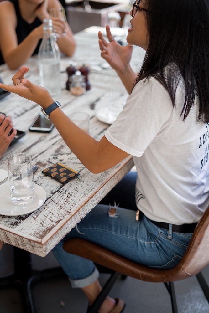 Femme à l'avant-plan qui discute avec d'autres gens attablés autour d'une table comme un client potentiel